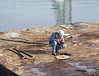 Figure 1: Shipyard Competent Person, with PFD, testing tanks on a barge prior to authorizing entry. Note: Fall protection to be installed after testing for initial entry