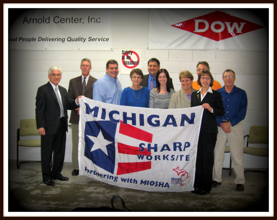 Arnold Center Inc. staff holding MIOSHA SHARP flag at SHARP award ceremony.